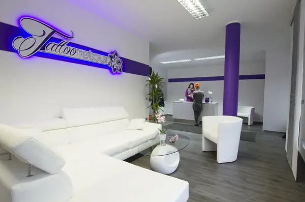 Modernes Tattooentfernungsstudio mit weißem Wartebereich, lila Akzenten und Empfangstresen.